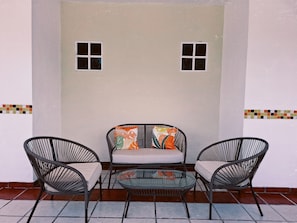 A patio with a sofa and two chairs, a glass table, and a tiled floor.