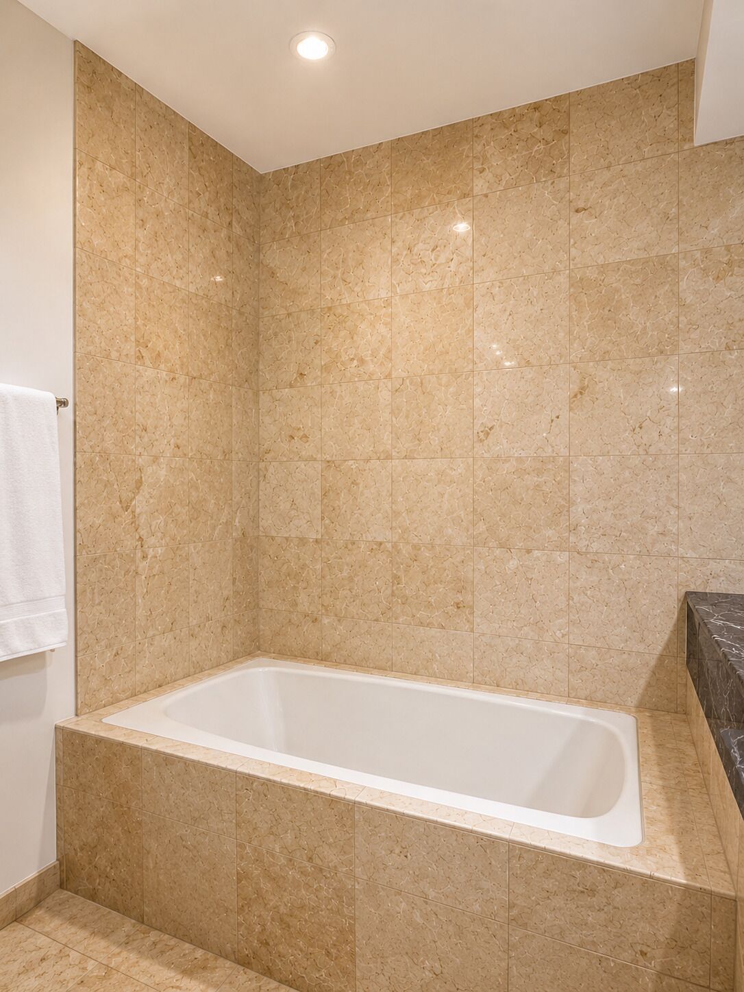 Uma casa de banho com banheira, paredes em azulejo e uma toalha branca num porta-toalhas.