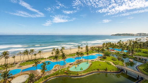 A resort with multiple swimming pools, a beach, palm trees, and a view of the ocean.