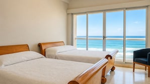 A room with two wooden beds, a view of the ocean, and a chair.
