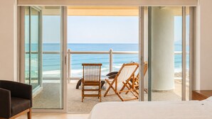 A room with a bed, a chair, and a view of the ocean through large glass doors.