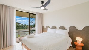 Une chambre avec un lit, un ventilateur de plafond, une vue par la fenêtre et un balcon.