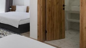 A bedroom with a bed, a wooden wardrobe, and a bathroom visible through a glass door.