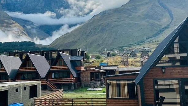 A mountain lodge with a view of snow-capped peaks and a valley below.