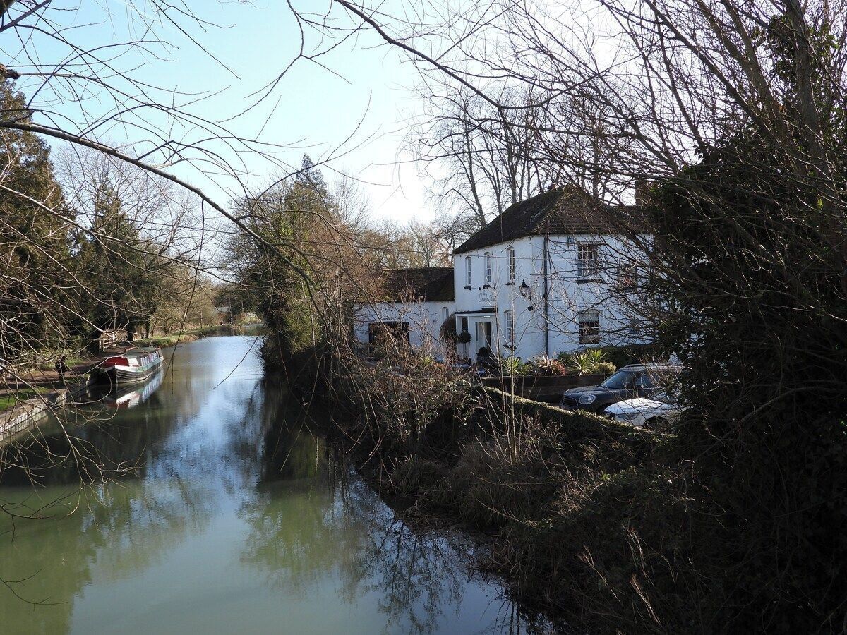 A river with a boat, a white building with a dark roof, and parked cars.