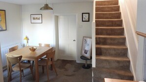 En matplats med ett träbord och stolar, en hängande lampa och en trappa med steg som är klädda med matta.