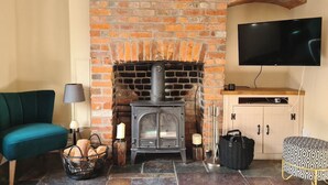 A cozy room with a brick fireplace, a flat-screen TV, a teal sofa, and a patterned ottoman. - Gorgeous 2 bedroom Kintbury cottage (Kintbury)