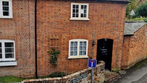 A brick building with a white door, a blue sign with a T symbol, and a brick wall with a nameplate. - Gorgeous 2 bedroom Kintbury cottage (Kintbury)