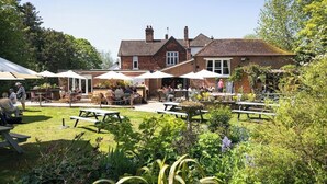 A brick building with outdoor seating and tables, surrounded by greenery. - Gorgeous 2 bedroom Kintbury cottage (Kintbury)