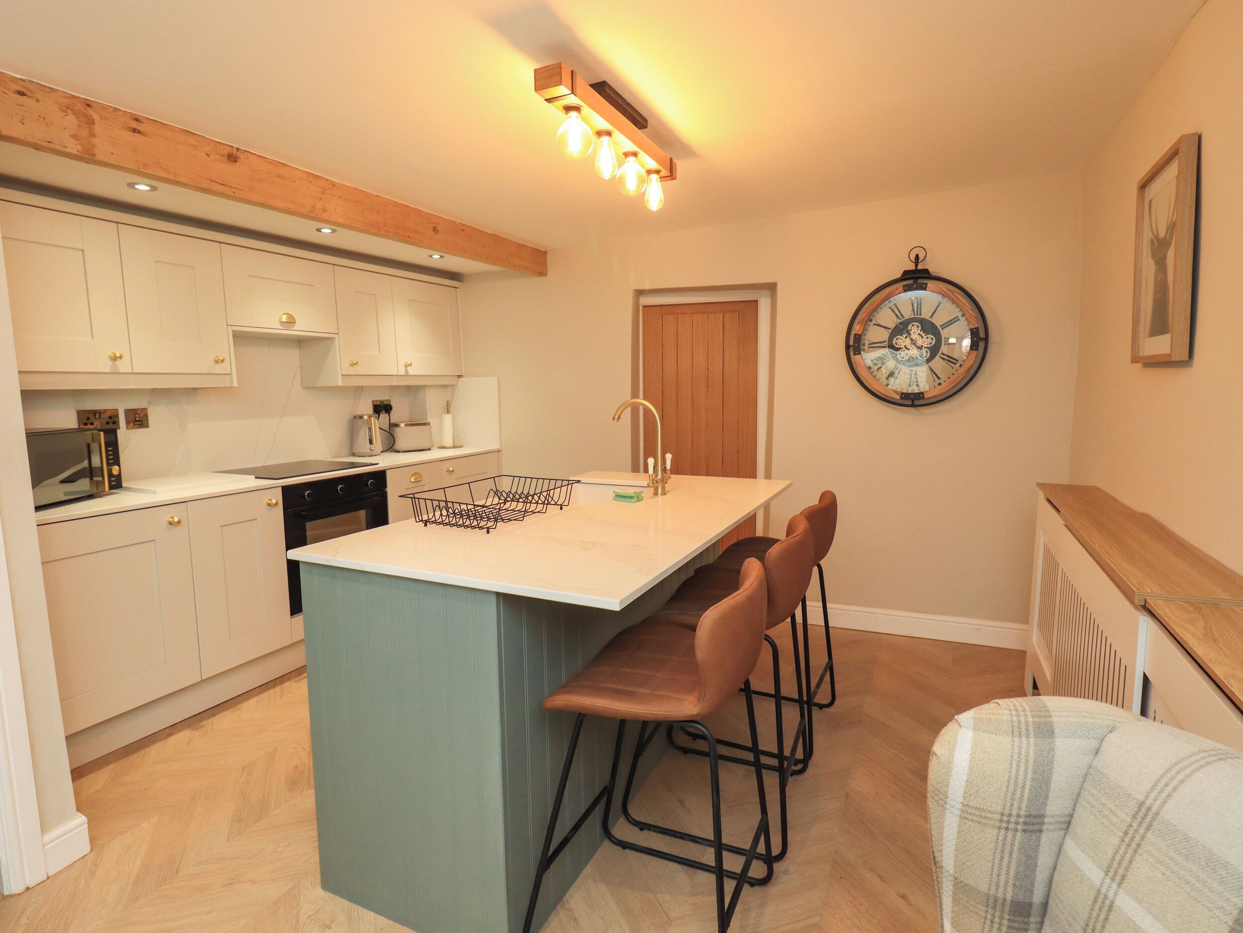 A kitchen with white cabinets, a wooden ceiling, a clock, and a bar stool.