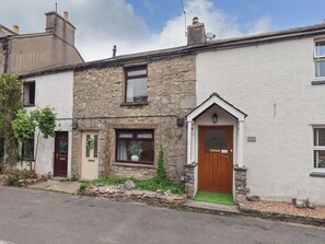 A stone house with a wooden door, a small window with a plant, and a sign reading 'WESTON COTTAGE.' - Dana House (Carnforth)