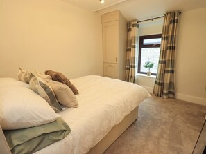 A bedroom with a bed, pillows, a window with curtains, a door, and a small plant on the windowsill. - Dana House (Carnforth)
