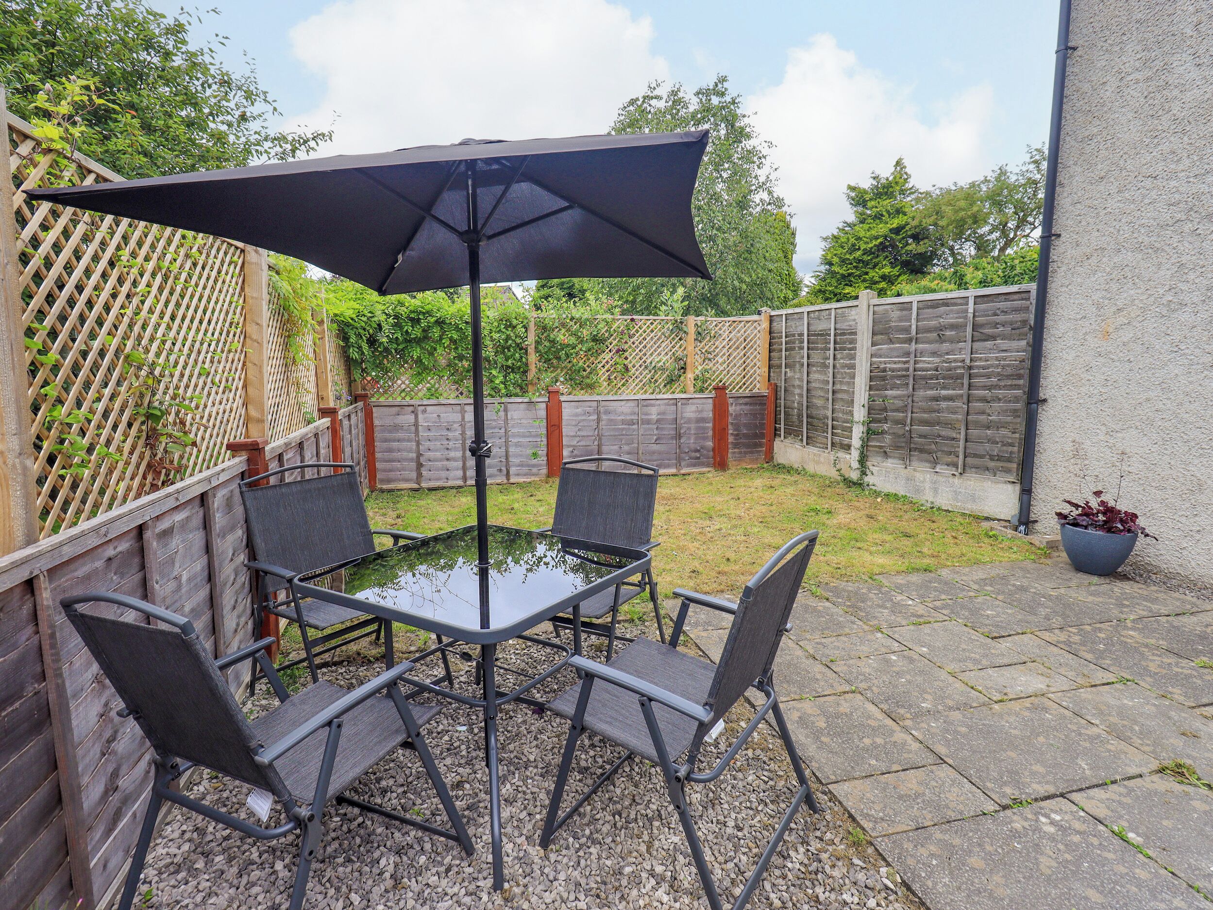 Une terrasse avec une table et des chaises, un parasol noir et une clôture en bois.