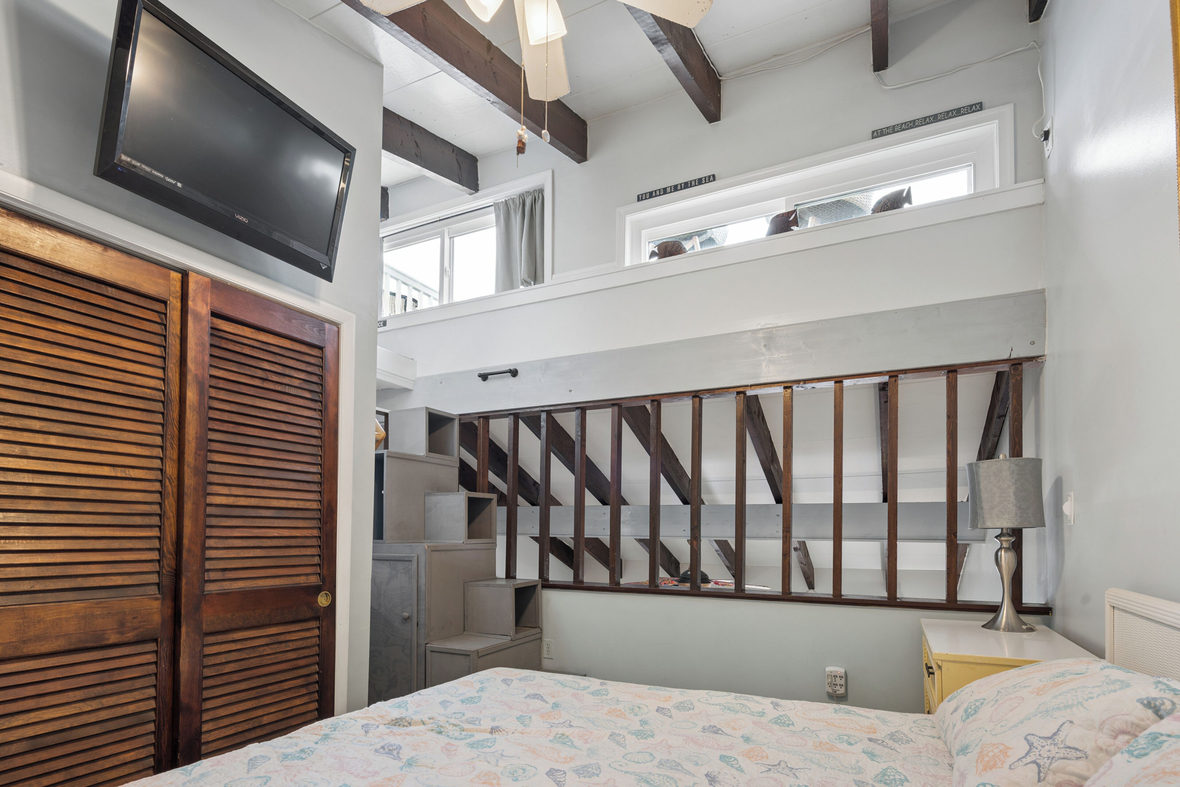 A bedroom with a bed, a TV mounted on the wall, a wooden door, and a staircase.