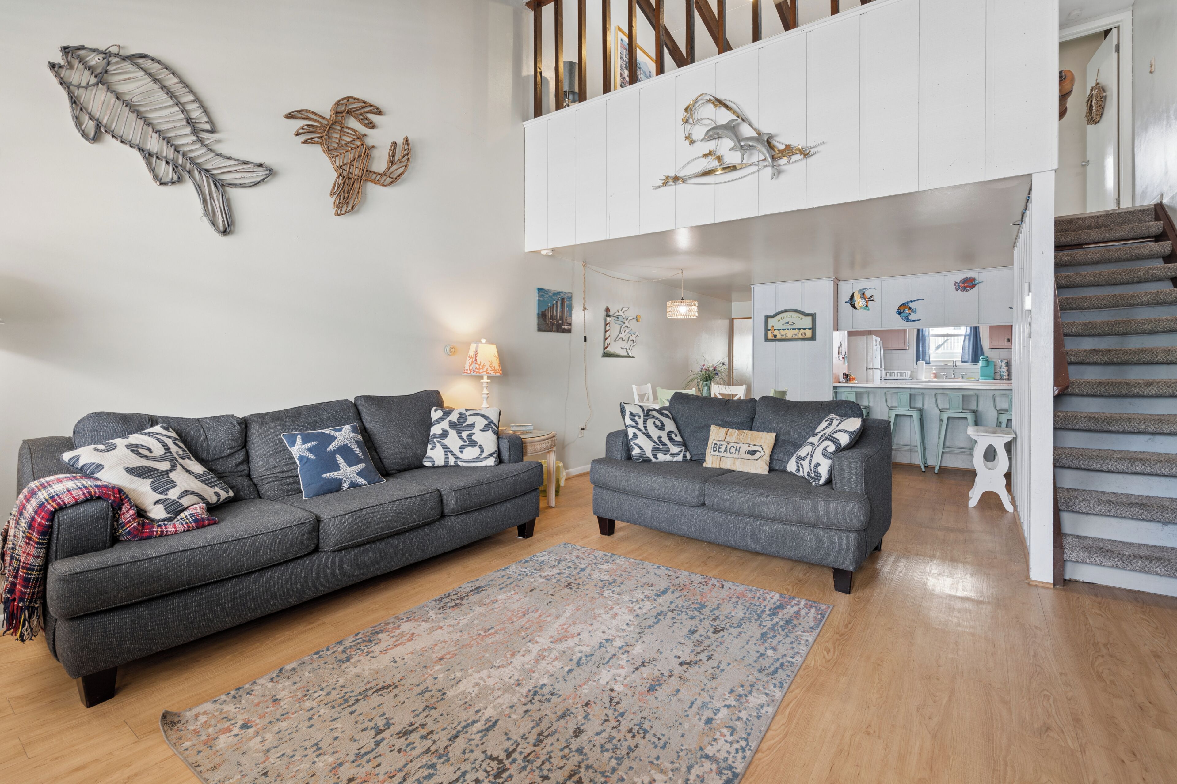 A living room with two grey sofas, a patterned rug, and wall art including a fish and a turtle.