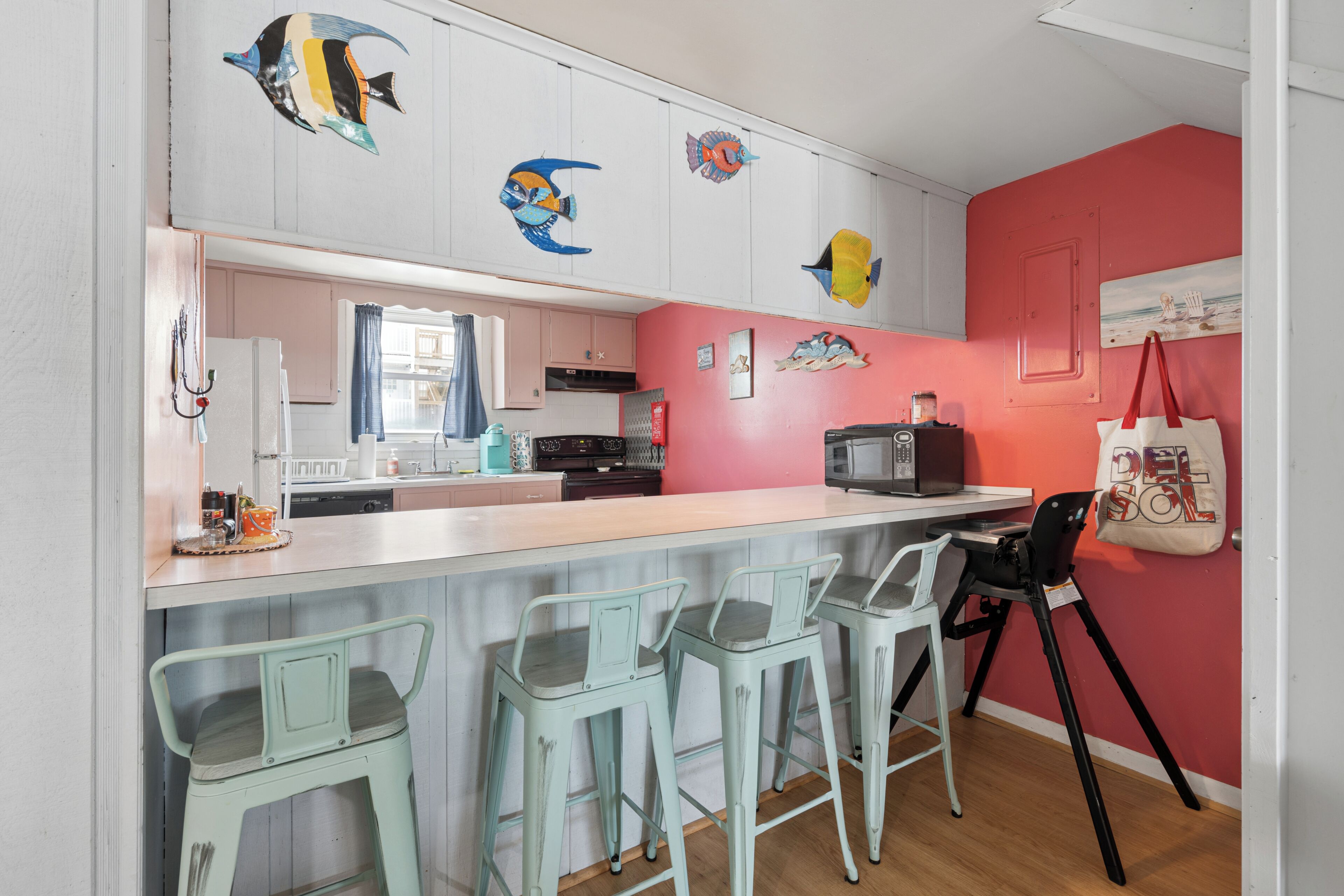 A kitchen with a bar area, bar stools, a microwave, and a red wall with fish decorations.