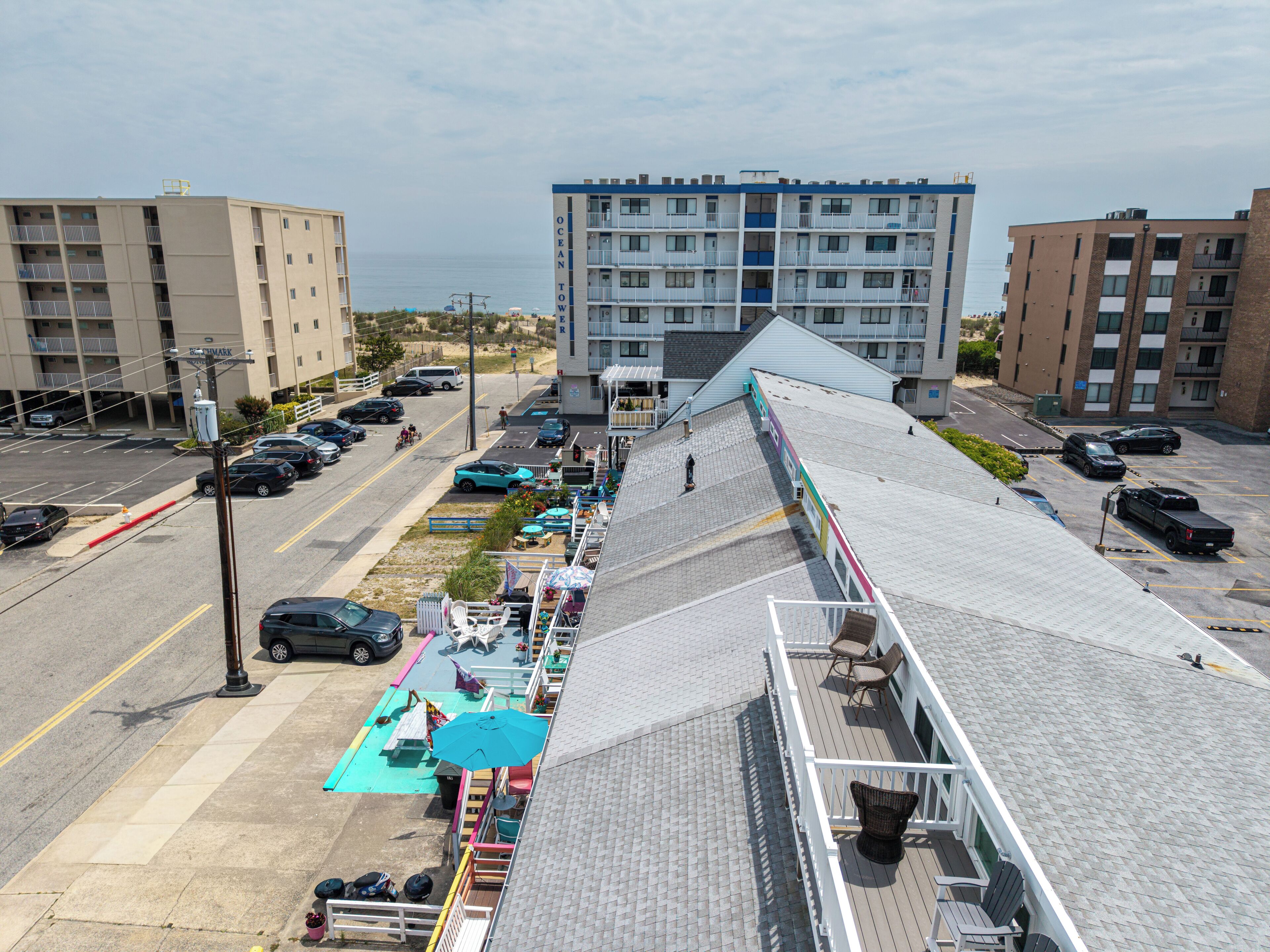 A multi-story building with a rooftop deck, a parking lot, and a view of the ocean.