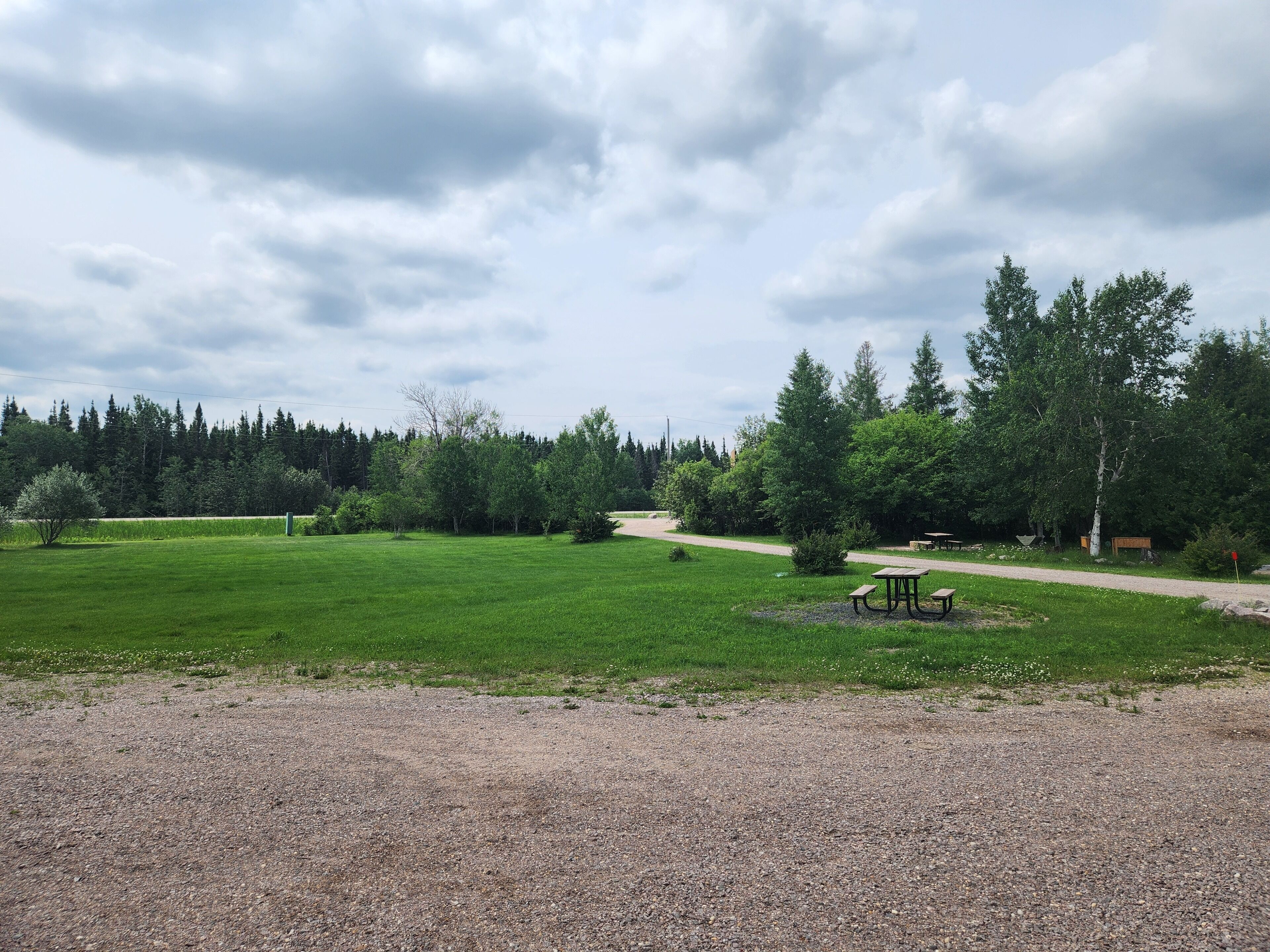 A gravel path leading to picnic tables in a grassy field with trees in the background.