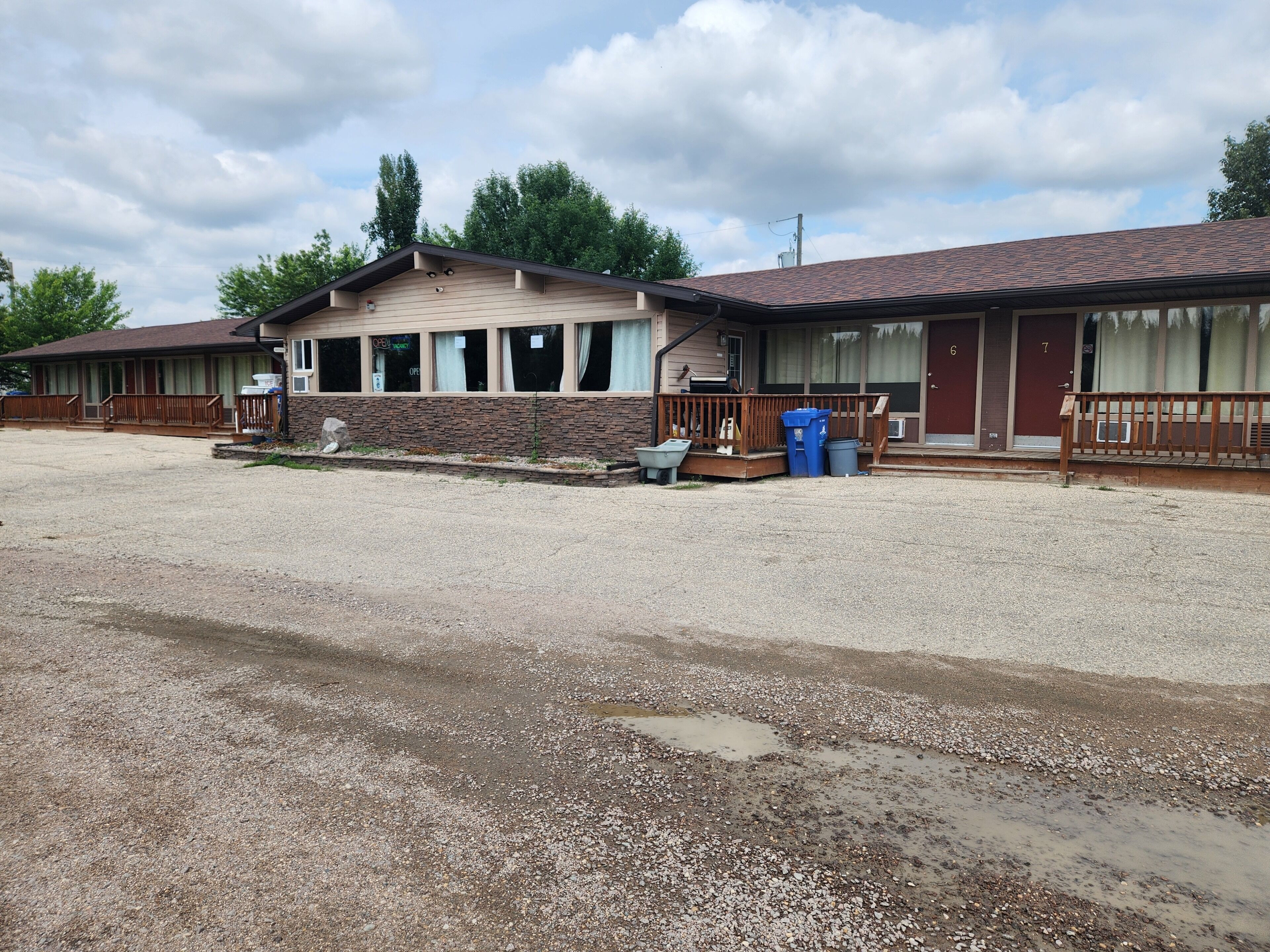 A motel with a gravel driveway, a wooden deck, and a stone facade.
