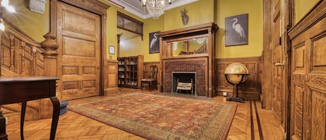 Una habitación con una puerta de madera grande, chimenea, un globo terráqueo y un candelabro.