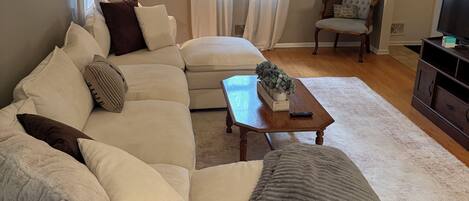 A living room with a sectional sofa, a coffee table, a chair, and a television.