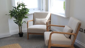 Ett rum med två beige fåtöljer, en krukväxt och en matta.