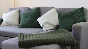 En grå soffa med tre kuddar i olika material och färger.