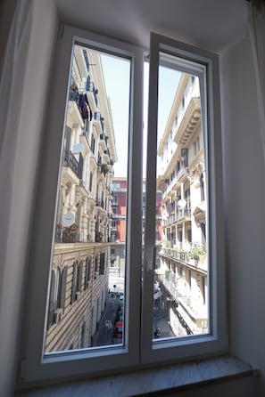A window with a view of a narrow street lined with multi-story buildings, balconies, and air conditioning units. - A little gem just a stone's throw from the sea in the heart of Naples (Napoli)