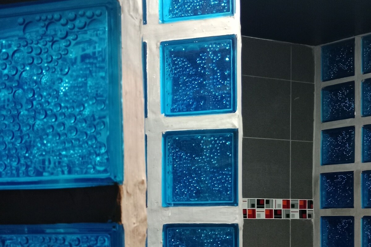 A bathroom with a tiled wall featuring square glass panels with water droplets.