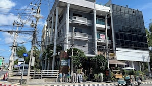 A multi-story building with a balcony on the second floor, a signboard with text, and a modern glass facade on the right. - HiSSS Style (Cha-am)
