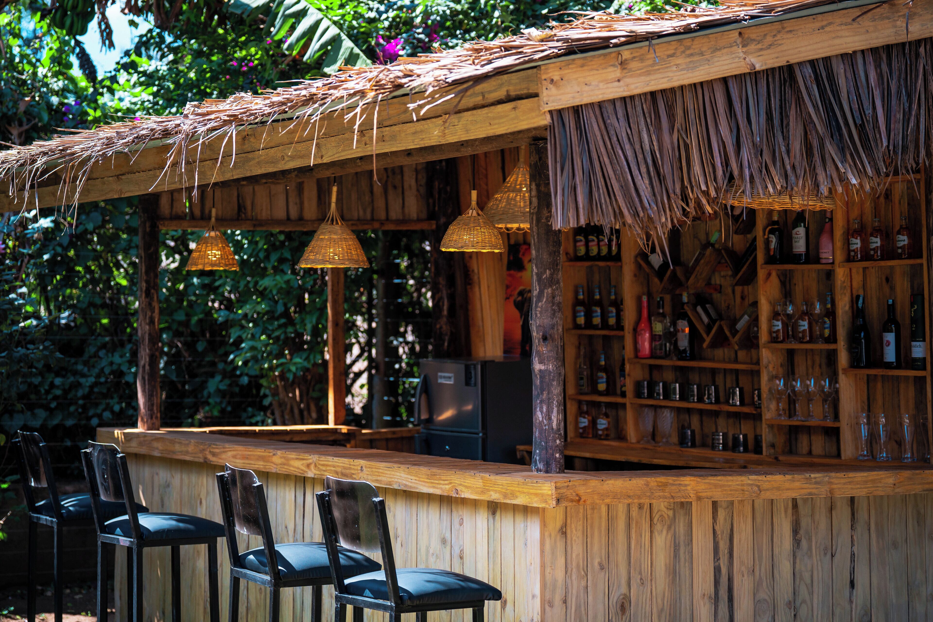 A wooden bar with thatched roof, wicker hanging lights, and a variety of bottles and glasses.