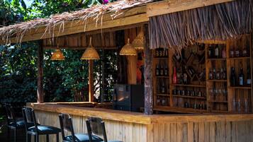 A wooden bar with thatched roof, wicker hanging lights, and a variety of bottles and glasses.