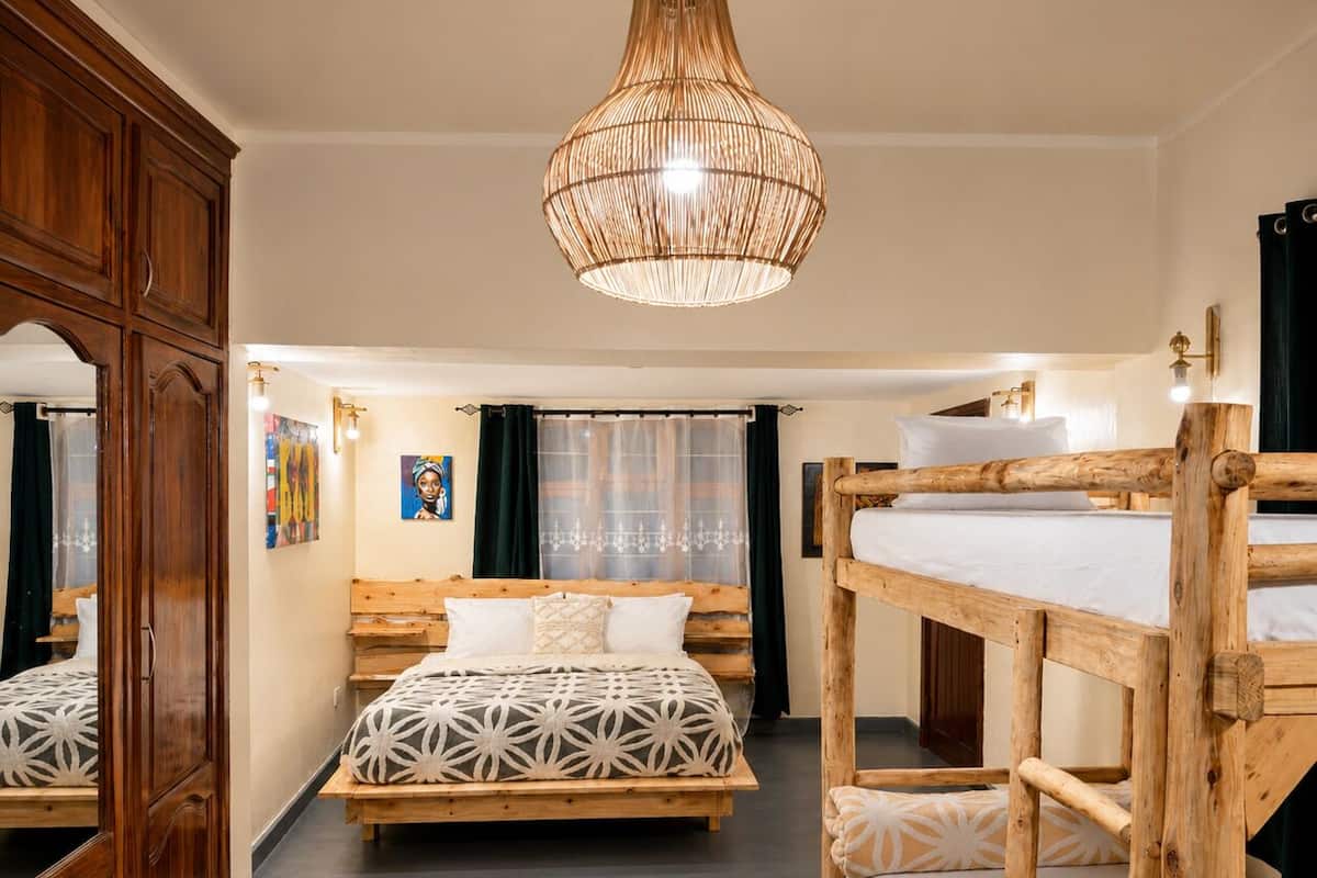 A room with a bunk bed, a wooden wardrobe, a hanging light fixture, and a bed with patterned bedding.