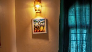 A room with two wooden chairs with green cushions, a small table, a woven rug, a wall-mounted light fixture, and a painting.