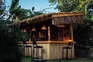 A wooden bar with a thatched roof, surrounded by greenery and equipped with hanging lights. - Hakuna matata villas & hostel (Arusha)