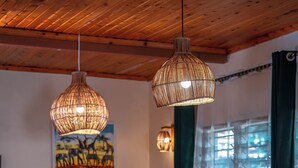 A wooden dining table with chairs, a hanging woven light fixture, and a painting on the wall.