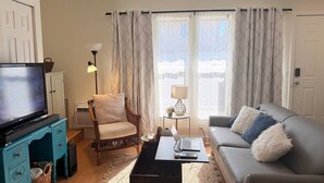Ett vardagsrum med en tv, soffa, fåtölj, soffbord, lampa och utsikt genom fönstret.