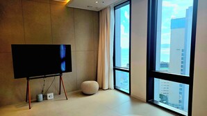 Een moderne hotelkamer met een groot raam, een flatscreen televisie op een standaard, een ronde tafel en een klein voetenbankje.