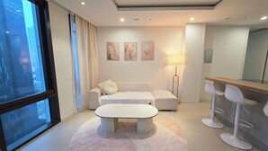 Een moderne hotelkamer met een groot raam, een bank, een ronde salontafel, een vloerlamp en een barretje.