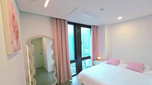 Een slaapkamer met een bed, een grote spiegel, een raam met gordijnen en uitzicht op de stad.