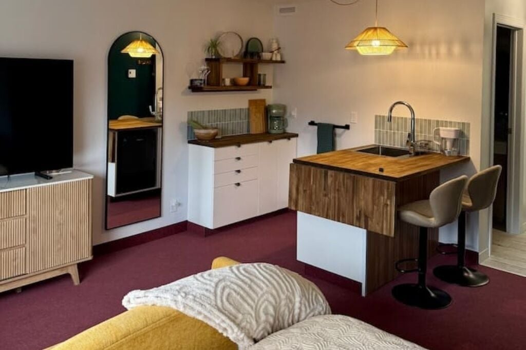 Een kleine leefruimte met kitchenette, een bed, een televisie en een spiegel.