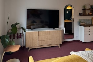 Una sala de estar con televisor, un mueble de madera, un espejo, una planta y un sofá amarillo.