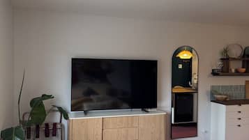 A modern living room with a flat-screen TV, a wooden cabinet, a mirror, and a yellow sofa.