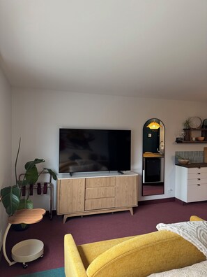 Un saló modern amb un televisor de pantalla plana, un armari de fusta, un mirall i un sofà groc.