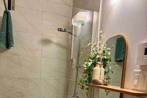 Un baño con ducha, un espejo y una estantería con una planta.
