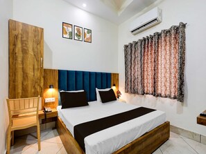 A bedroom with a wooden headboard, a bed with white and black bedding, a nightstand with a lamp, and a wall-mounted air conditioner. - Suite Hotel Paras Inn (Amritsar)