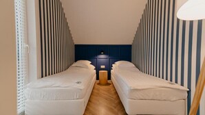 Una habitación pequeña con dos camas individuales, una mesita y una lámpara.