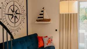 Una habitación con un sofá azul, un adorno de pared con forma de brújula, un estante con forma de velero rayado y una lámpara.