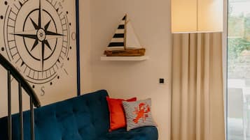 A room with a blue sofa, a compass wall decoration, a striped sailboat shelf, and a lamp.