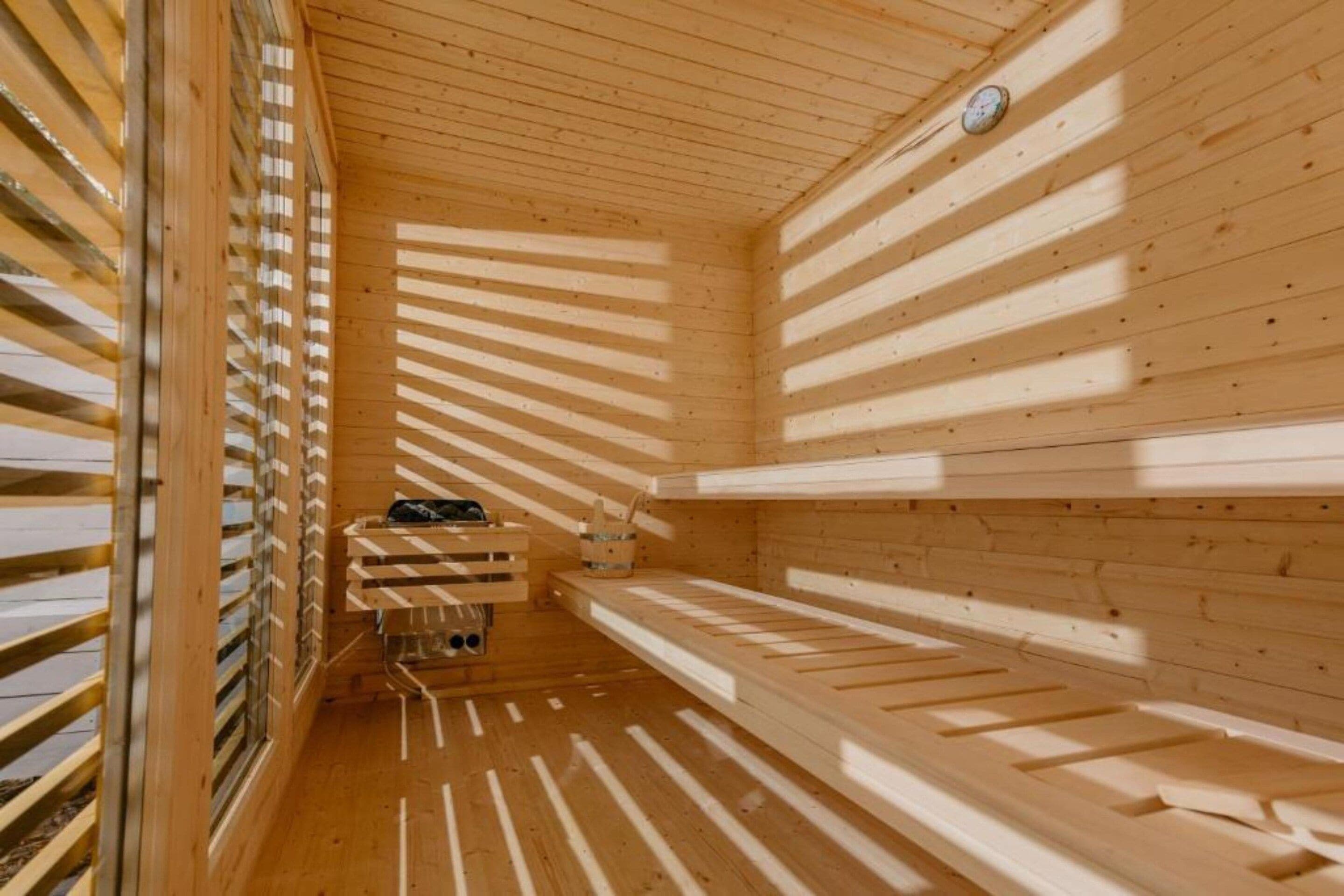A sauna with wooden slats on the walls and ceiling, a bench, and a small table with a bucket.
